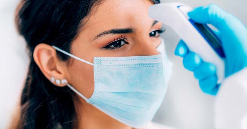 Woman with face mask getting temperature check.